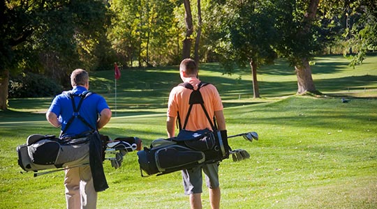 2 mannen met golftassen op een golfbaan
